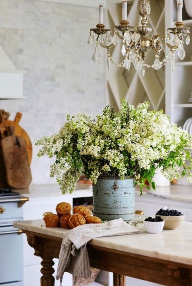 Białe kwiaty, proste emaliowane naczynie i żyrandol w... kuchni...