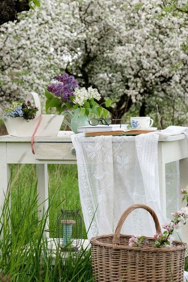 Stary, biały kuchenny stół, książka, bzy i piękny sad w tle...