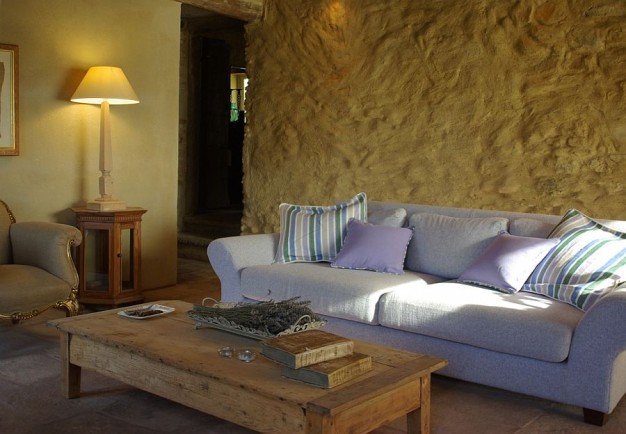 Lawendowa kanapa świetnie wygląda na tle kamiennej ciepłej ściany...